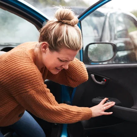 A young woman getting out of her car and holding her neck in pain after an accident
