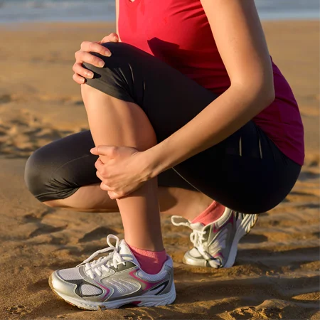 A runner crouched on the beach holding their leg and knee in pain