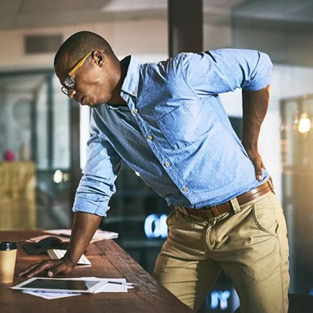 A man at the office bending over and holding his lower pack in pain