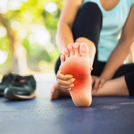 A woman holding her foot. Pain is indicated using red highlighting on the bottom of her foot